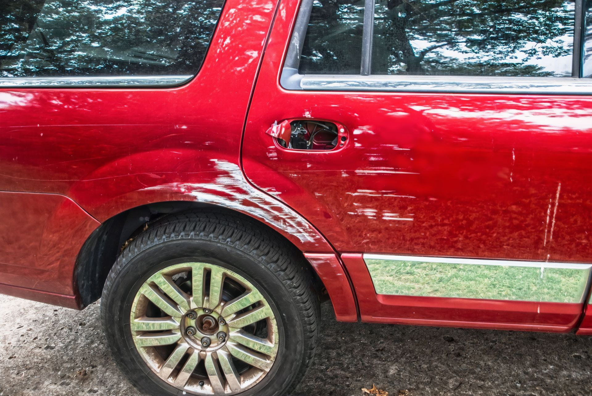 Red SUV side view with rear wheel and silver trim on a gravel driveway