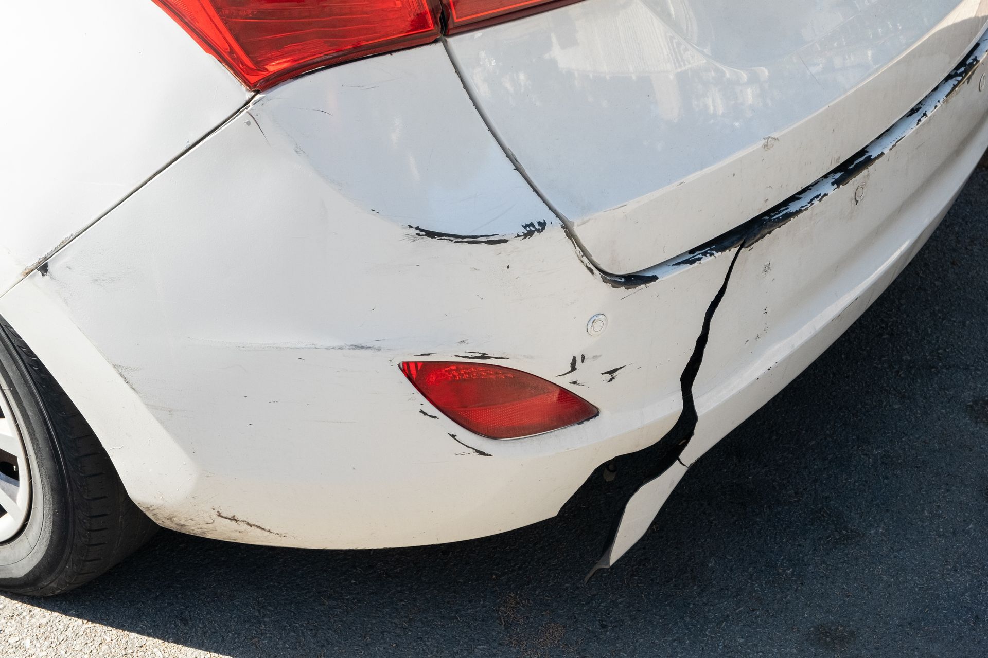 Rear of a white car with a large cracked and dented bumper after a collision