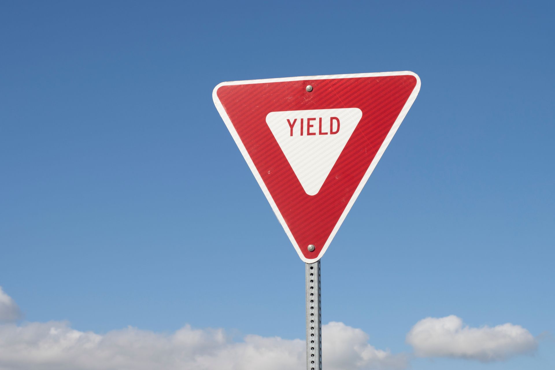 Red and white yield traffic sign against a blue sky