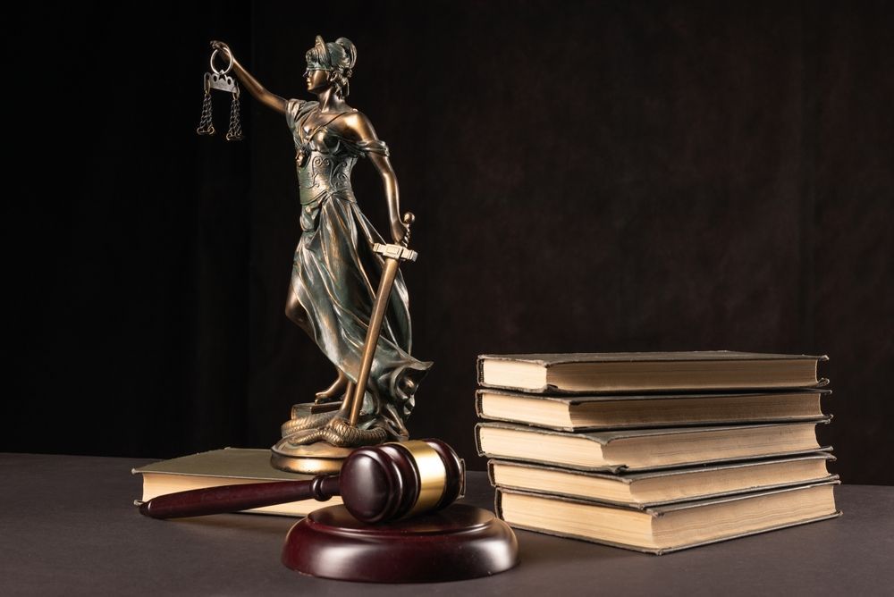 Lady Justice statue beside gavel and stacked law books on a dark background