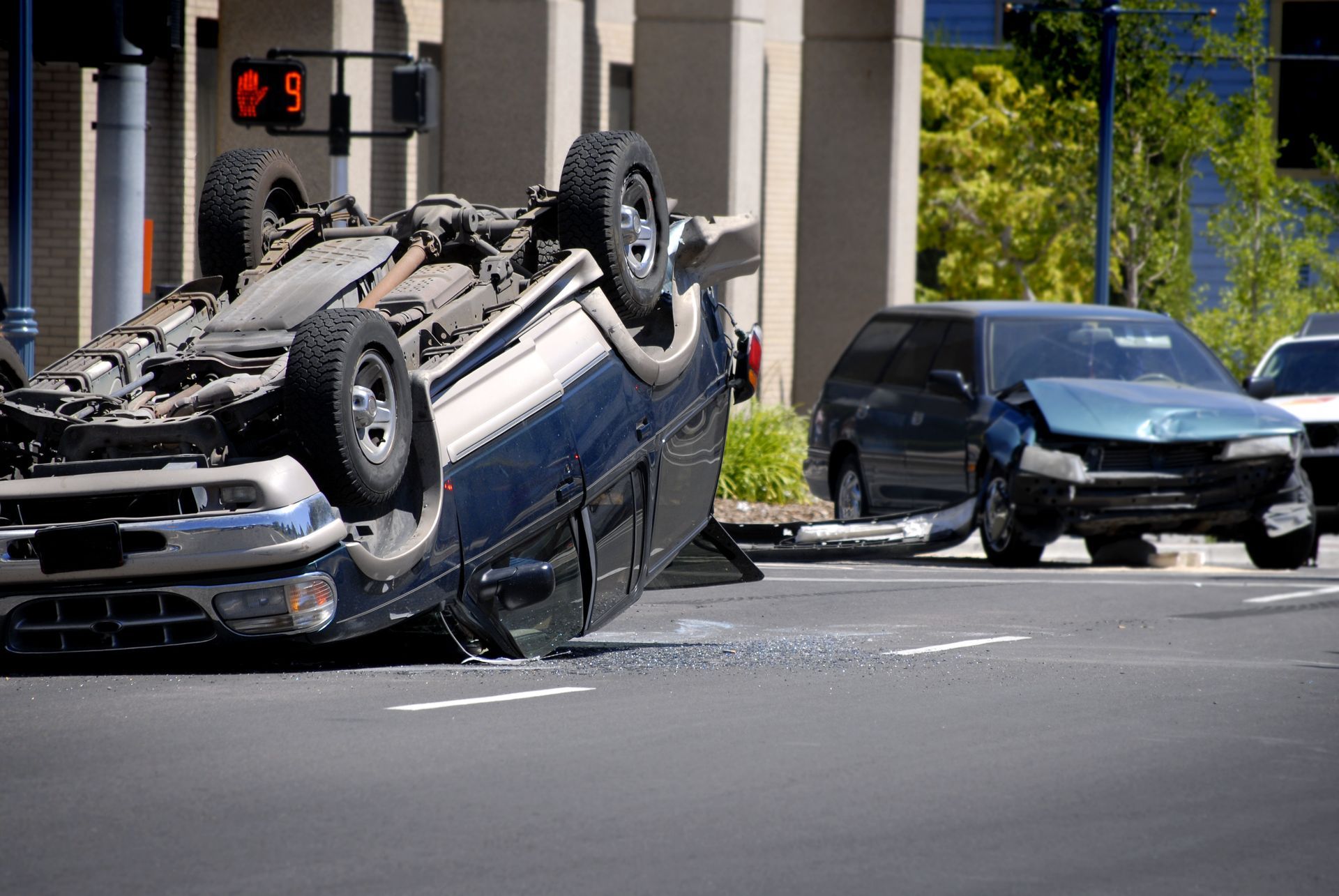 Overturned blue SUV in street crash, with a damaged black car nearby and debris on the road.