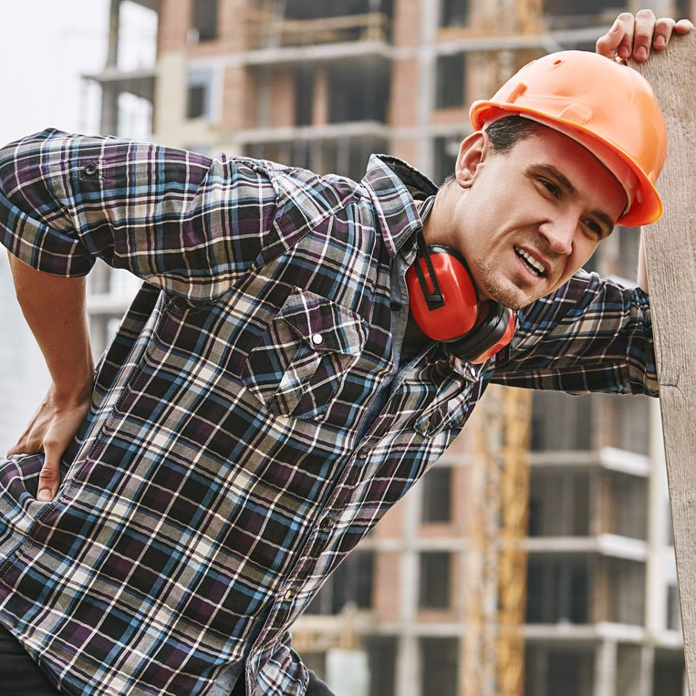 Construction worker in orange hard hat and red earmuffs, leaning forward at a building site.