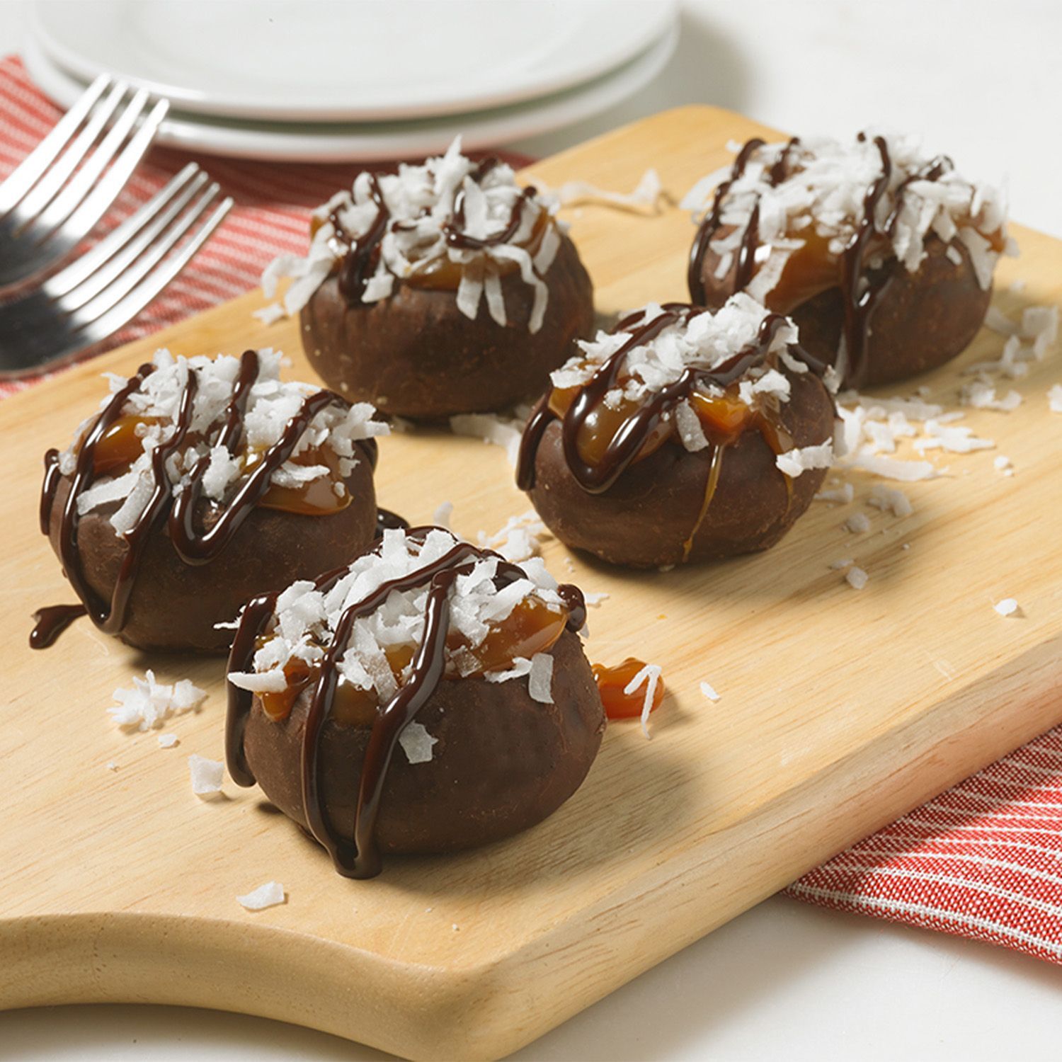 frosted mini donuts topped with coconut flakes on a wooden board and drizzled with chocolate and caramel sauce