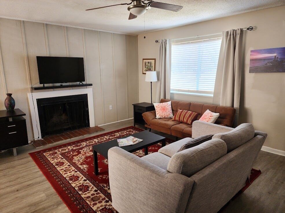 Living room with beige sofa, fireplace, red rug, TV, and window with blinds