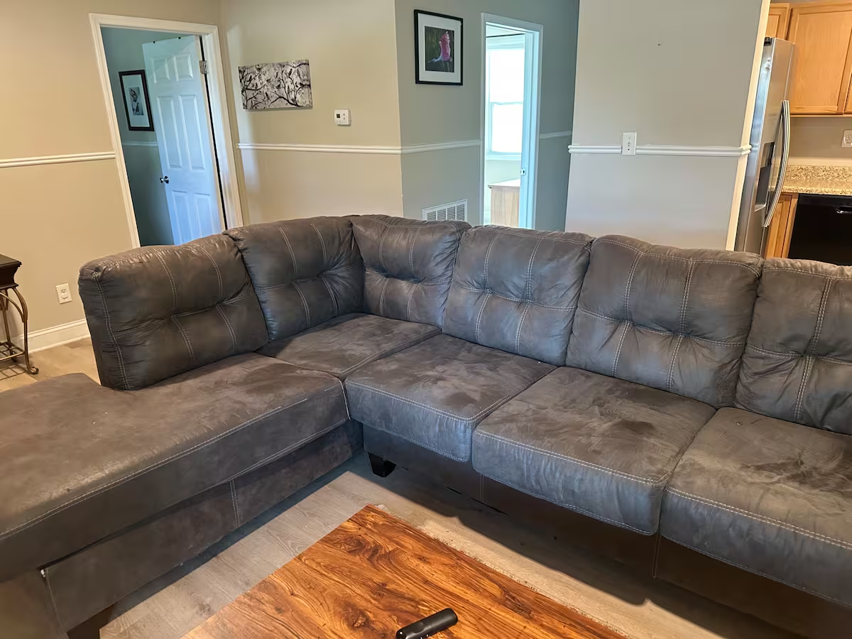 Gray L-shaped sectional sofa in a beige living room with wood flooring and a window door in back