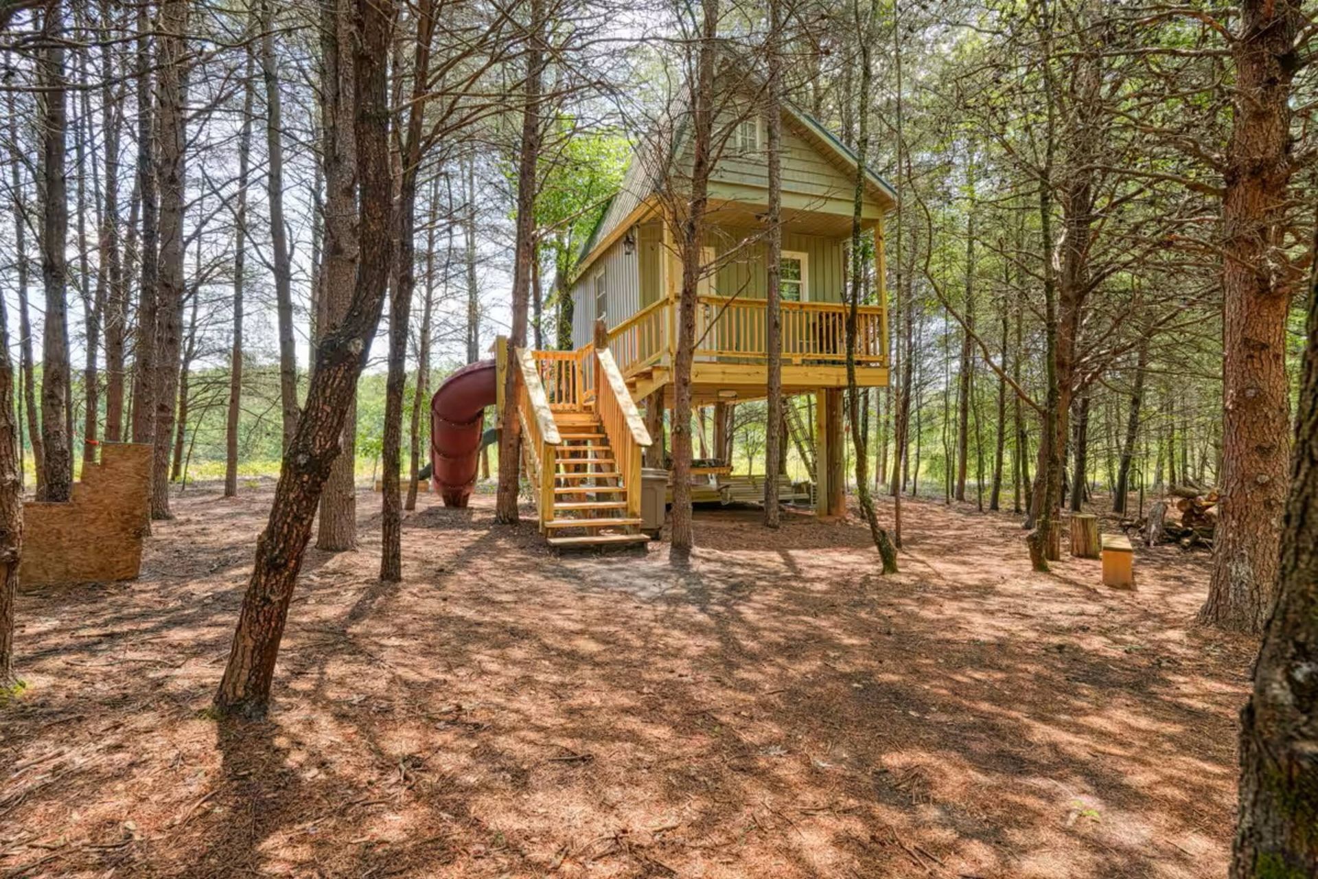 Yellow treehouse with stairs in a wooded forest clearing