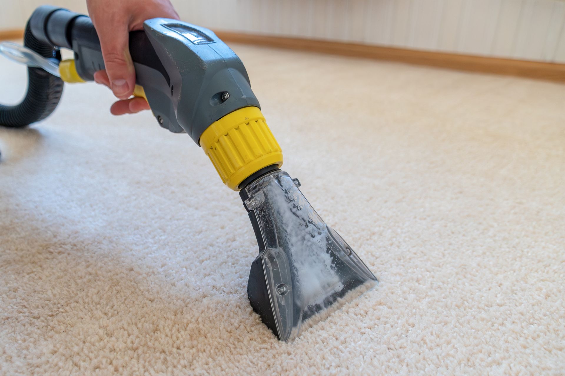Handheld carpet cleaner extracting dirt from a light beige carpet