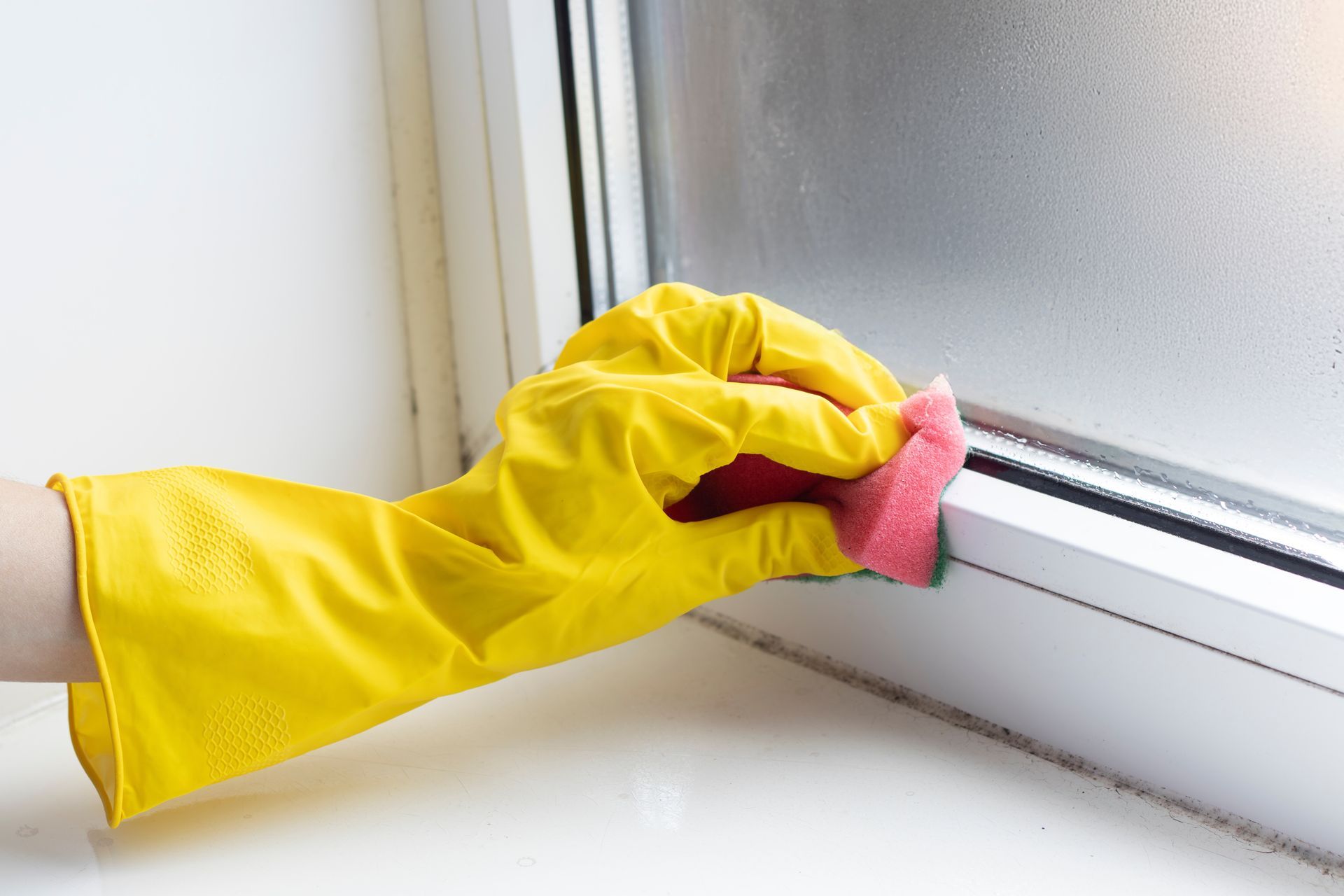 Gloved hand cleaning a window frame with a pink cloth