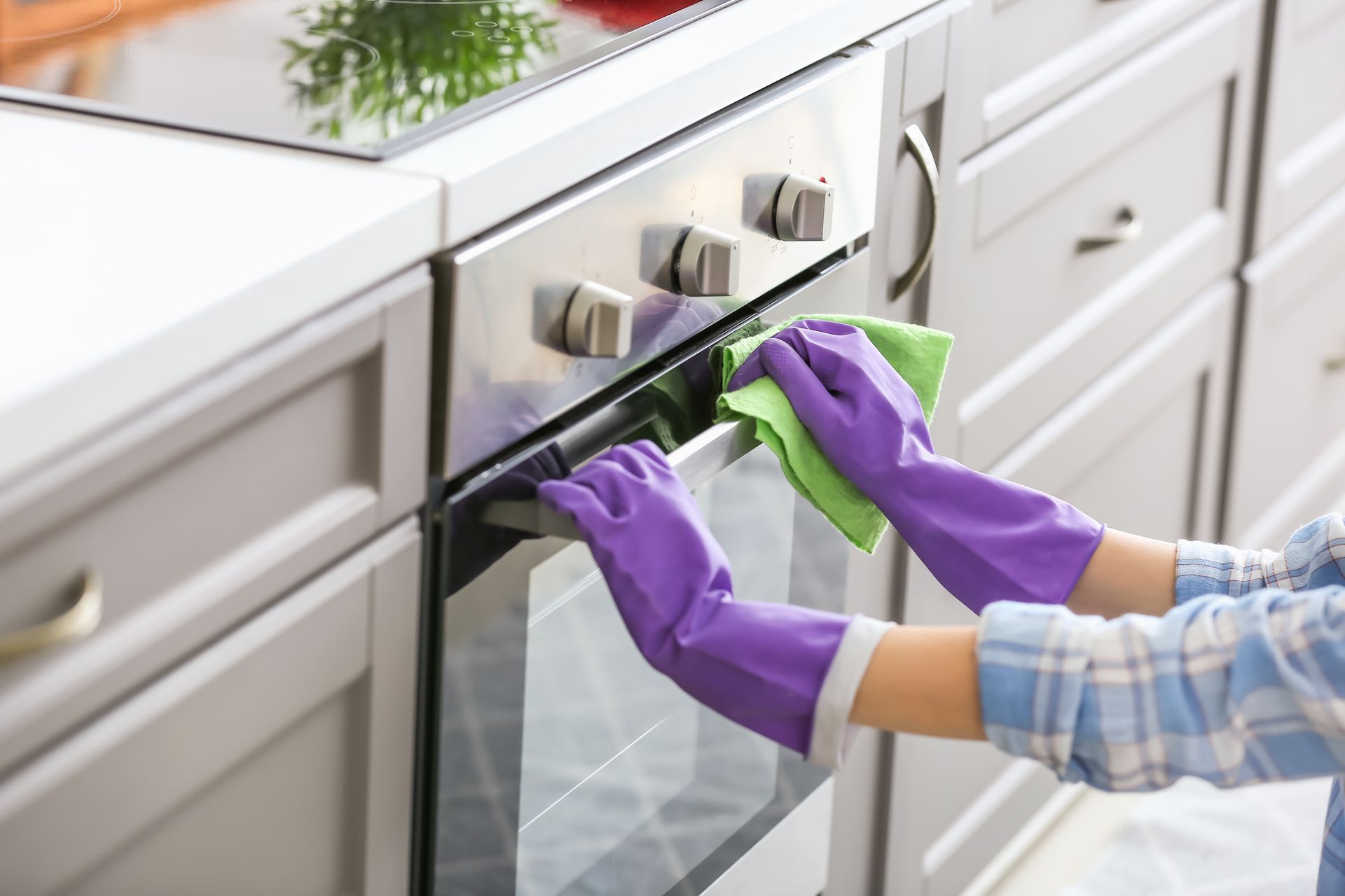 Purple-gloved hands cleaning a white oven with a green cloth in a kitchen