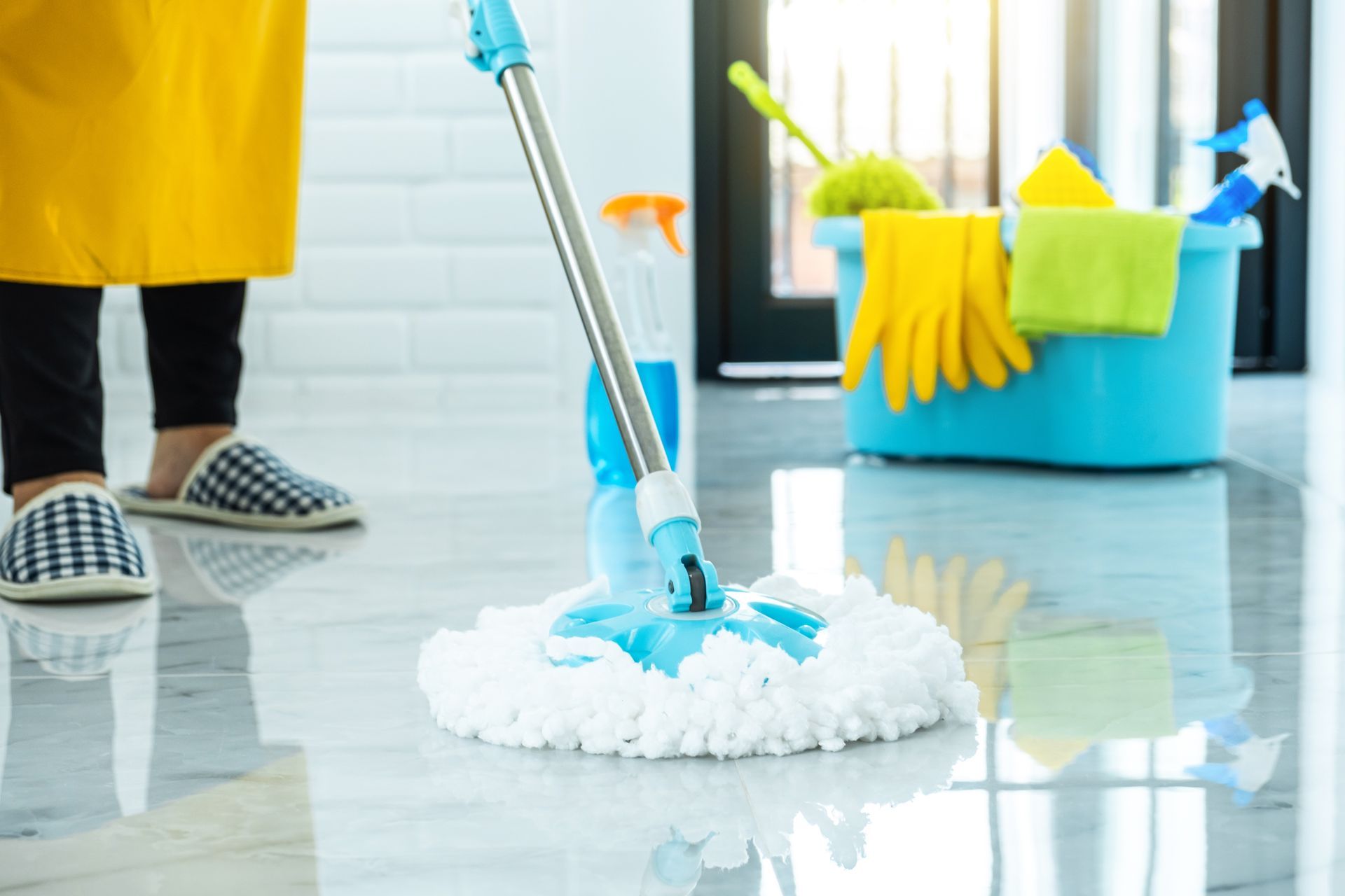 Mop cleaning a shiny floor beside a bucket of cleaning supplies and gloves