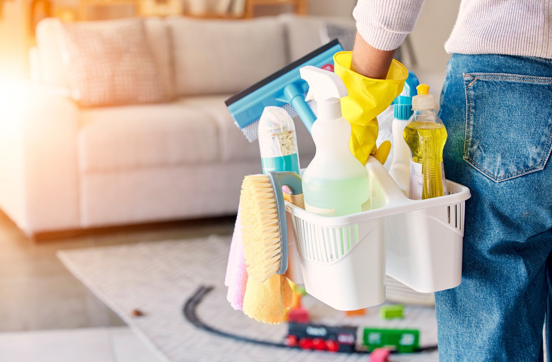 Person cleaning with a white caddy of supplies and yellow gloves in a living room