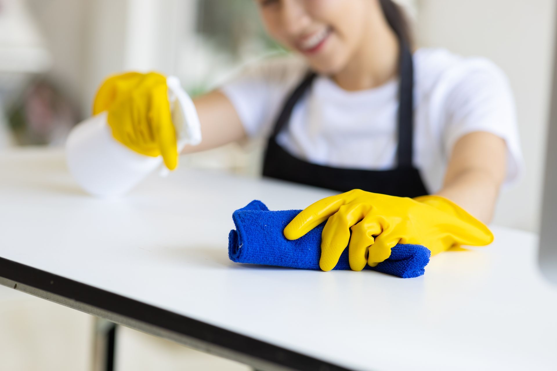 Person in yellow gloves wiping a white table with a blue cloth