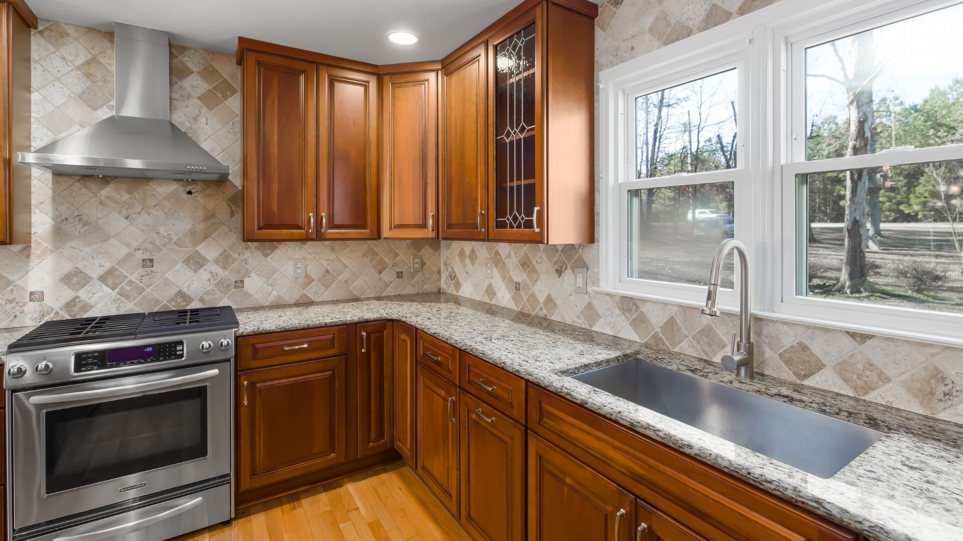 Bright kitchen with wooden cabinets, stainless steel stove, tiled backsplash, and a window over the sink.