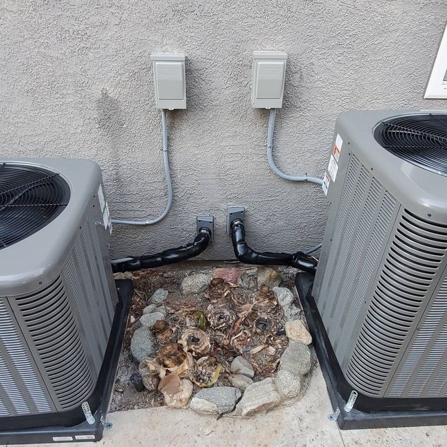 Outdoor central air conditioning unit beside a house, surrounded by landscaping stones and grass