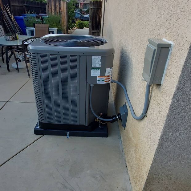 Outdoor air conditioner unit beside a house, surrounded by grass and landscaping.