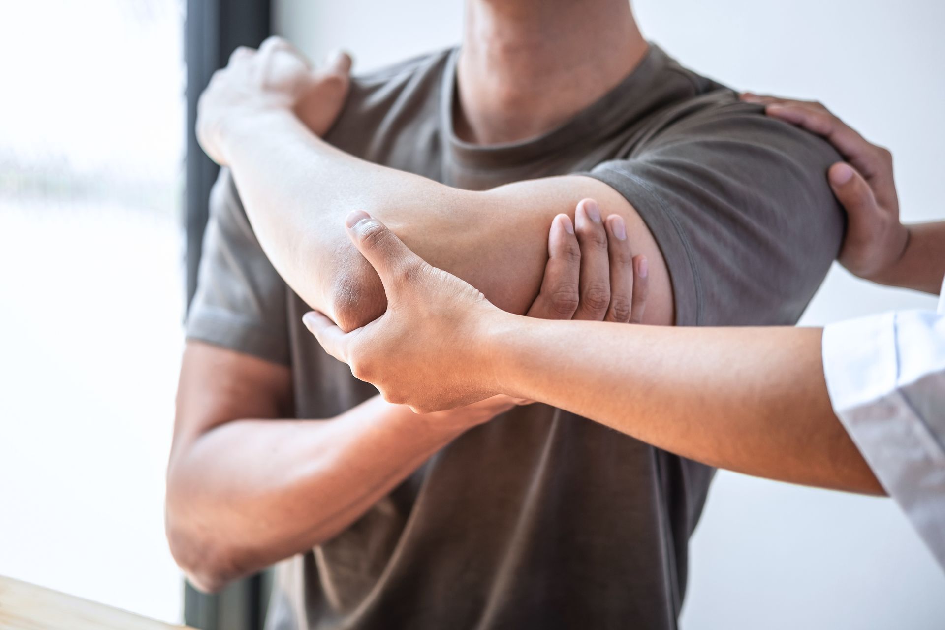 A physiotherapist is treating an injured arm of an athlete male patient.