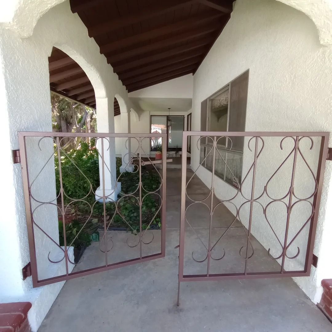 Open rusty gate leading to a covered porch with white columns and tiled floor
