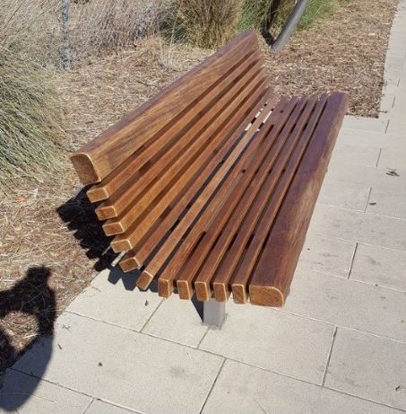 Wooden park bench with dark slats on a paved path beside dry grass