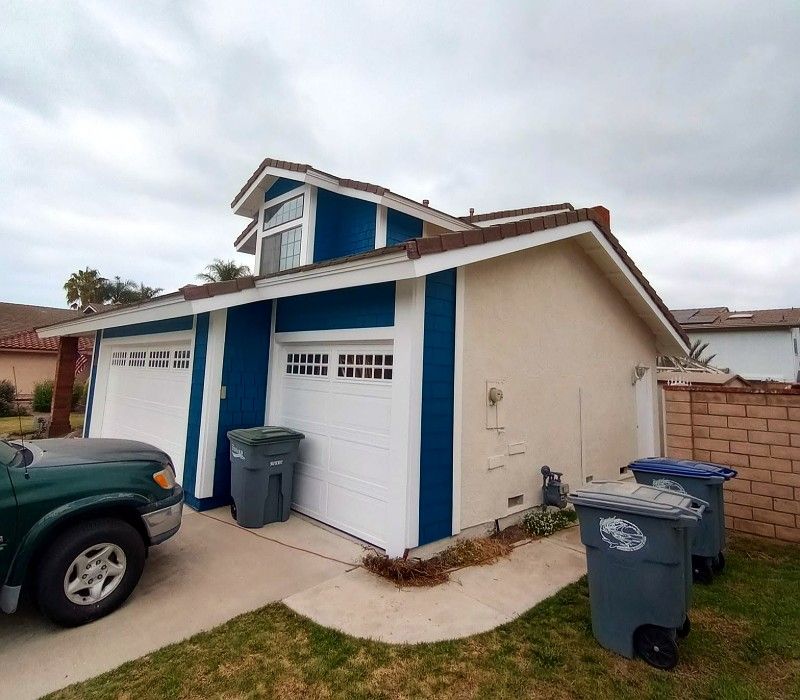 Suburban house garage with blue trim, two trash bins, and a parked car in the driveway