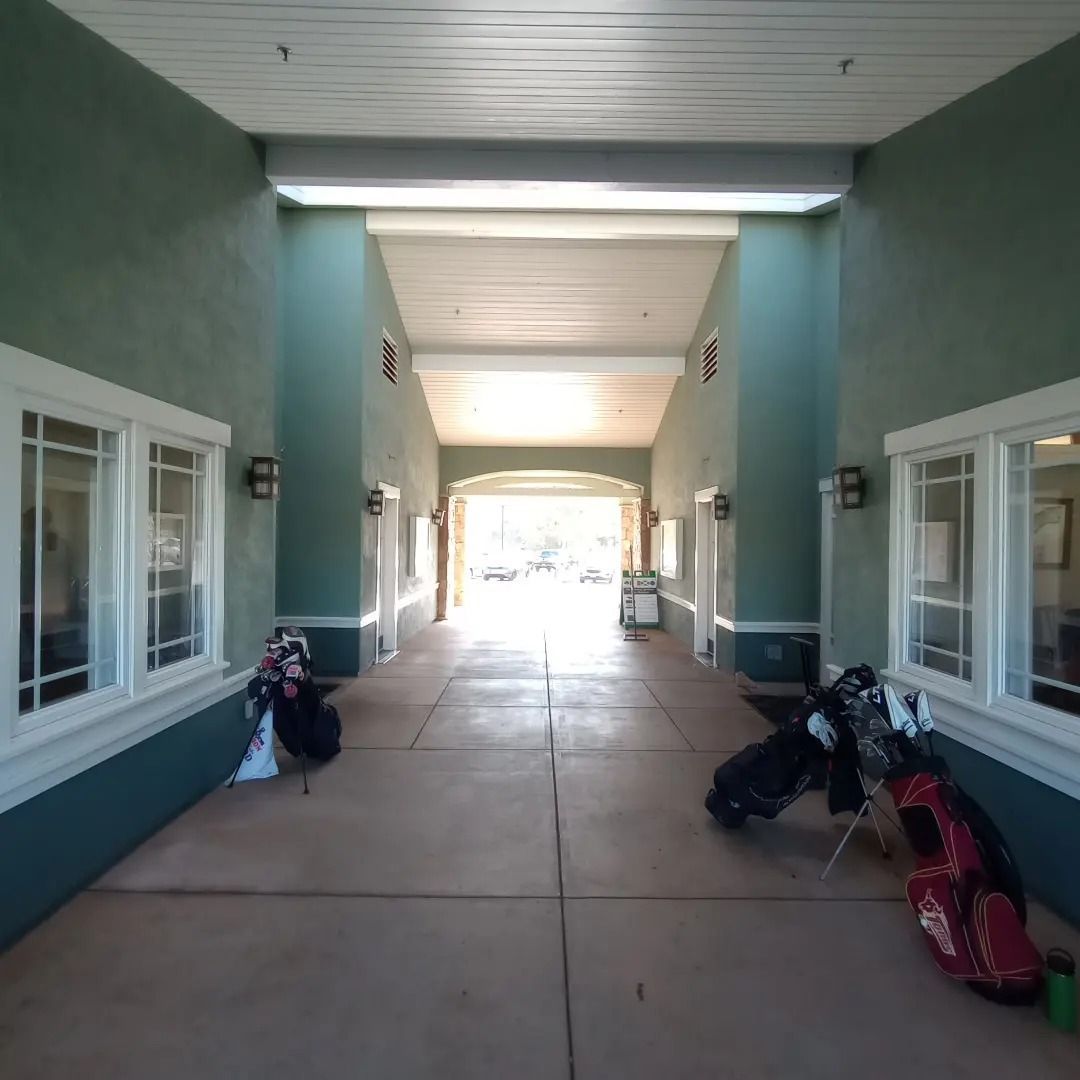 Covered walkway with green walls, windows, and several golf bags leaning against both sides