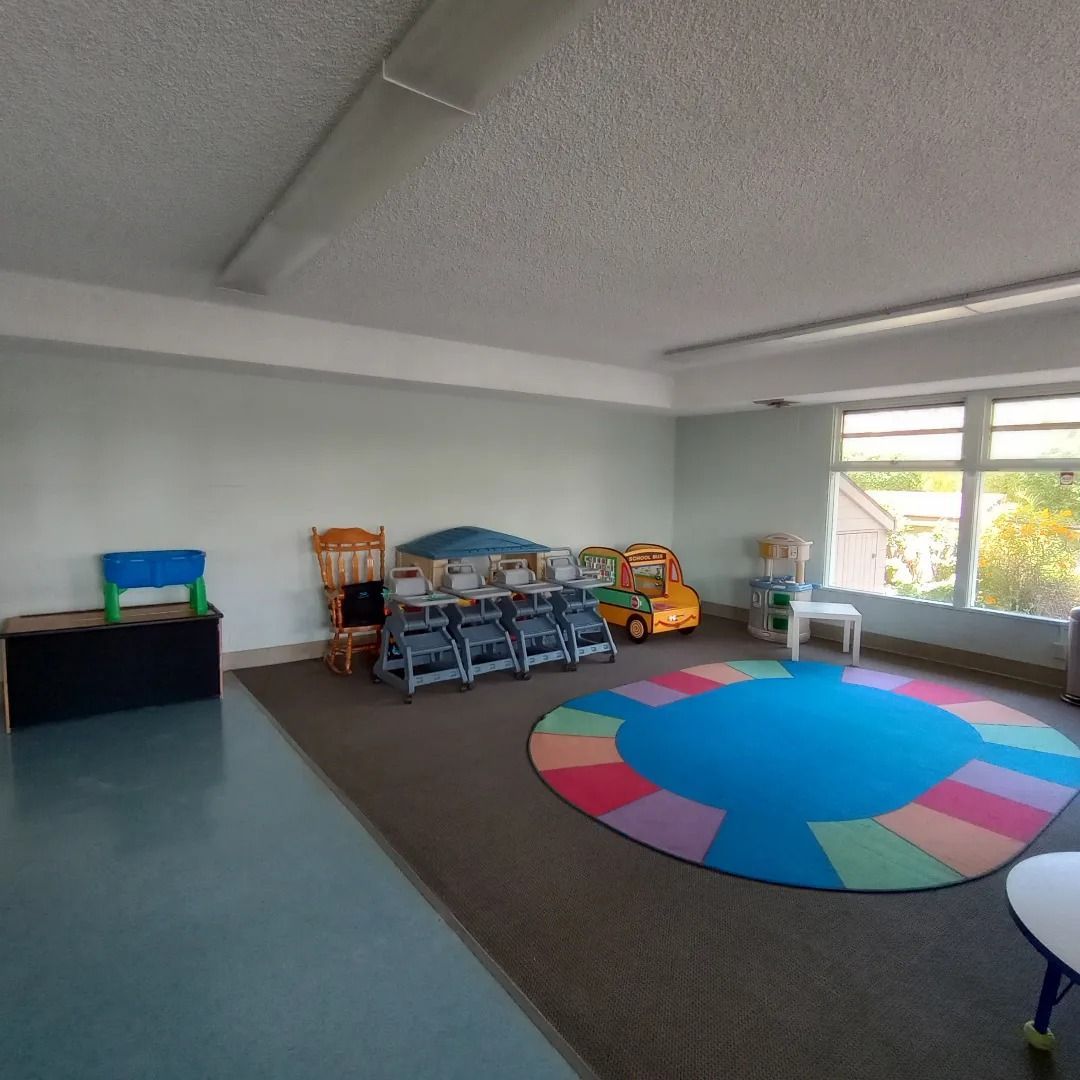 Empty classroom with colorful round rug, small chairs, toys, and large window light