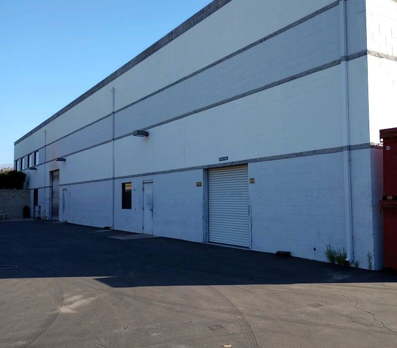 Large white industrial warehouse with loading bays and a paved parking lot under a clear blue sky
