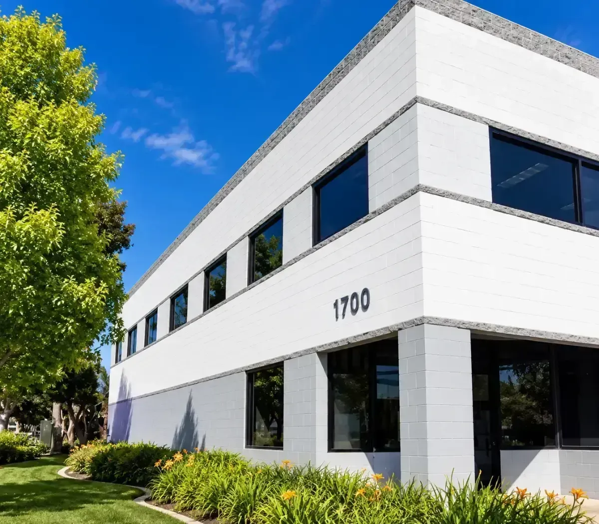 Modern white office building with black windows and the number 1700, beside trees and landscaping