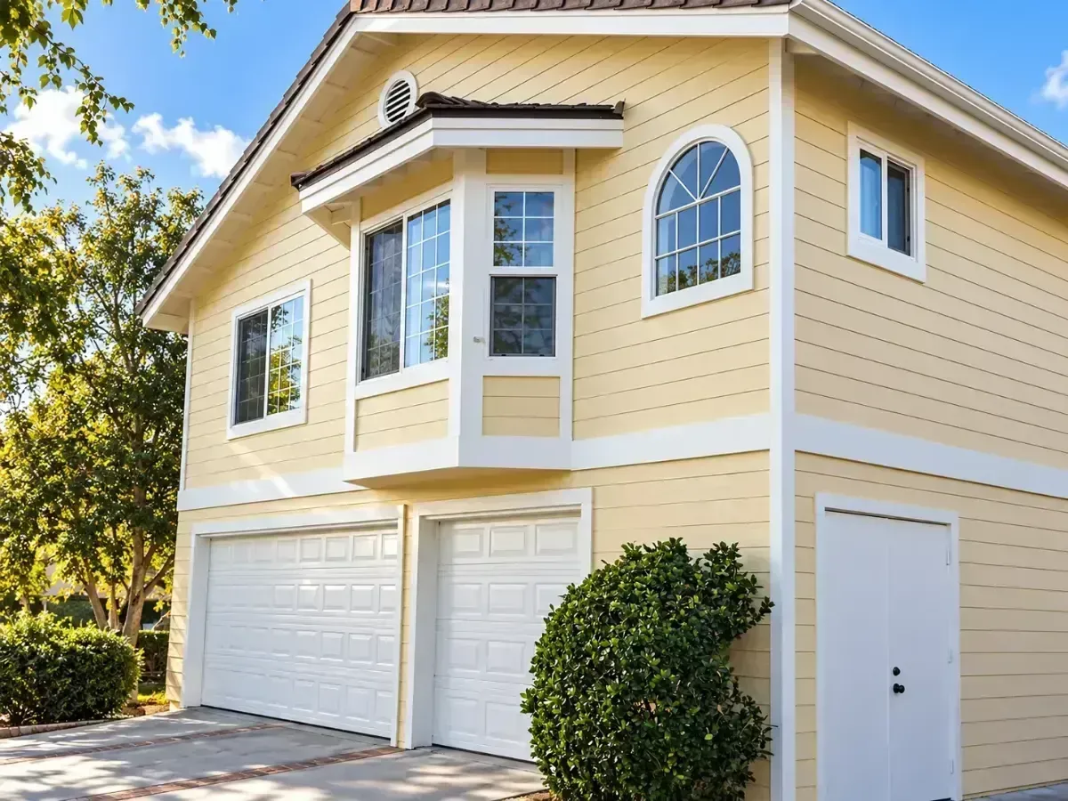 Two-story yellow house with white trim, garage doors, and a small side entry under a clear sky