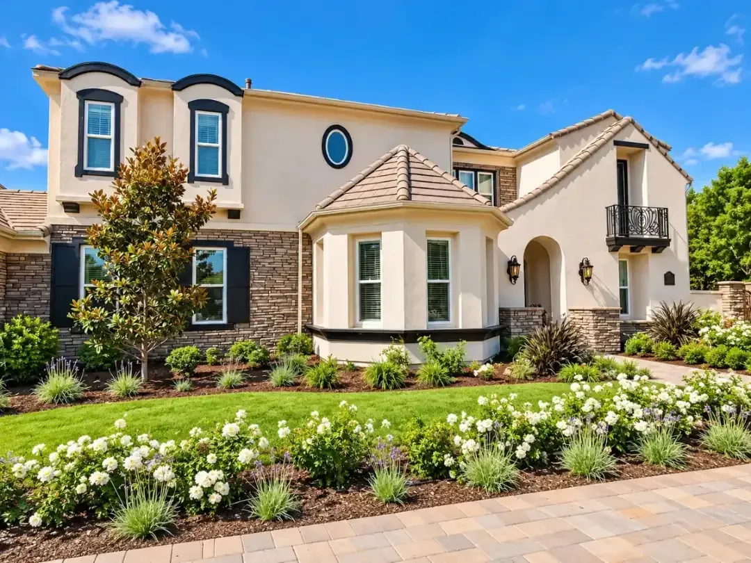 Large beige house with blue trim, landscaped front garden, and stone walkway under a clear blue sky