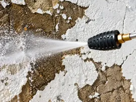 Garden hose nozzle spraying water against a peeling white wall