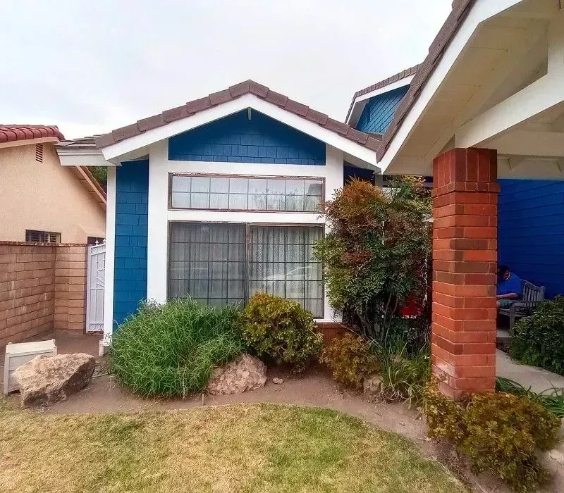 Small suburban house with blue trim, front window, brick pillar, and a landscaped yard