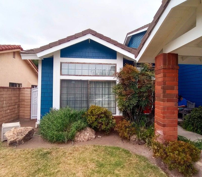 Single-story house with blue trim, brick columns, and a small front garden
