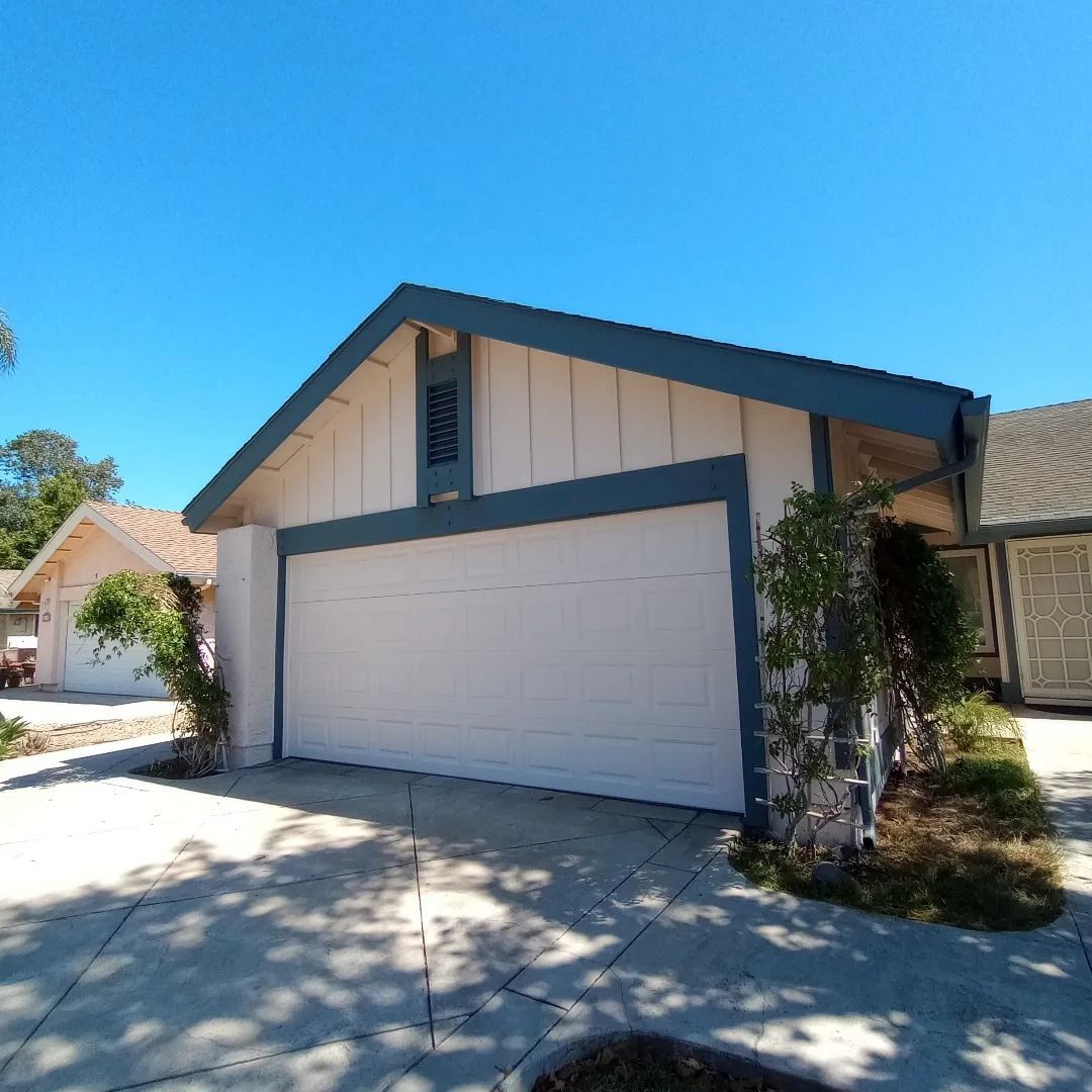 Suburban house with a white garage door, blue trim, and bright sunny driveway
