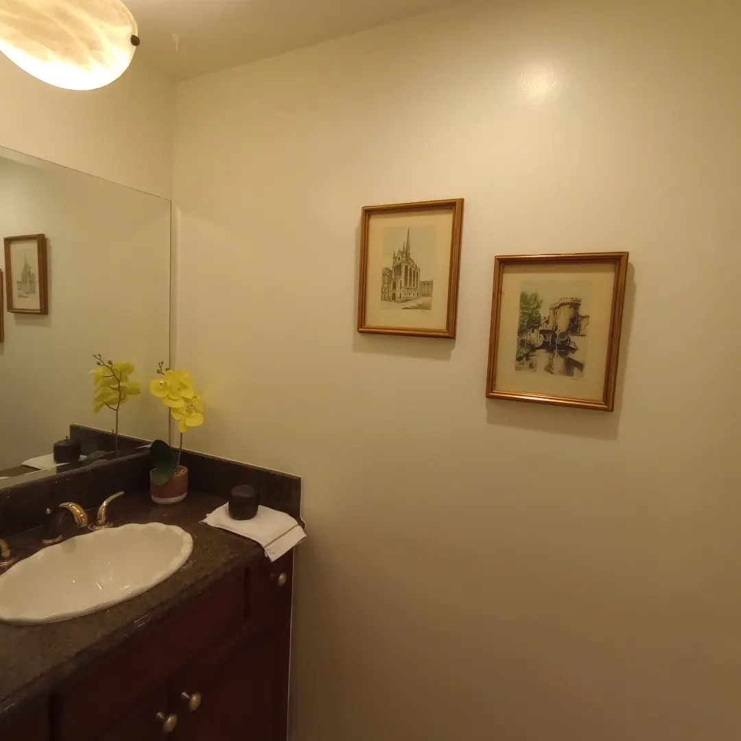Small bathroom with a sink, mirror, flowers, and two framed pictures on a beige wall.