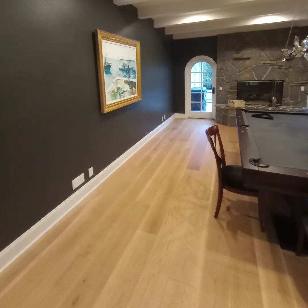 Empty dining room with dark walls, light wood floor, framed painting, and stone fireplace