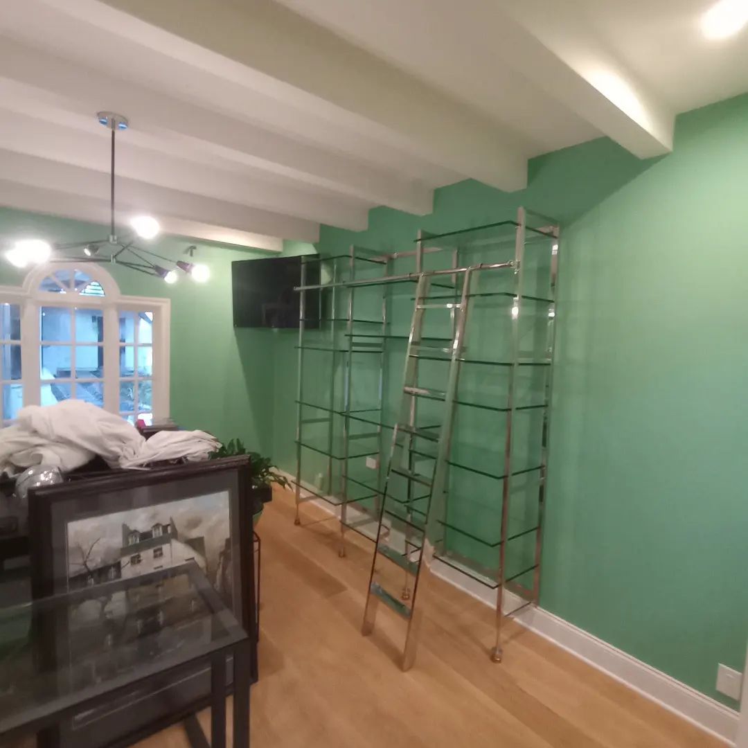 Renovation room with green walls, ladders, scaffolding, and a black cabinet near windows.