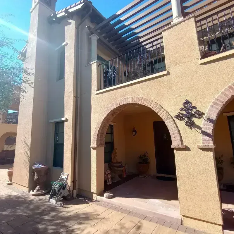 Sunlit stucco courtyard with arched patio openings and pergola beams over the entrance