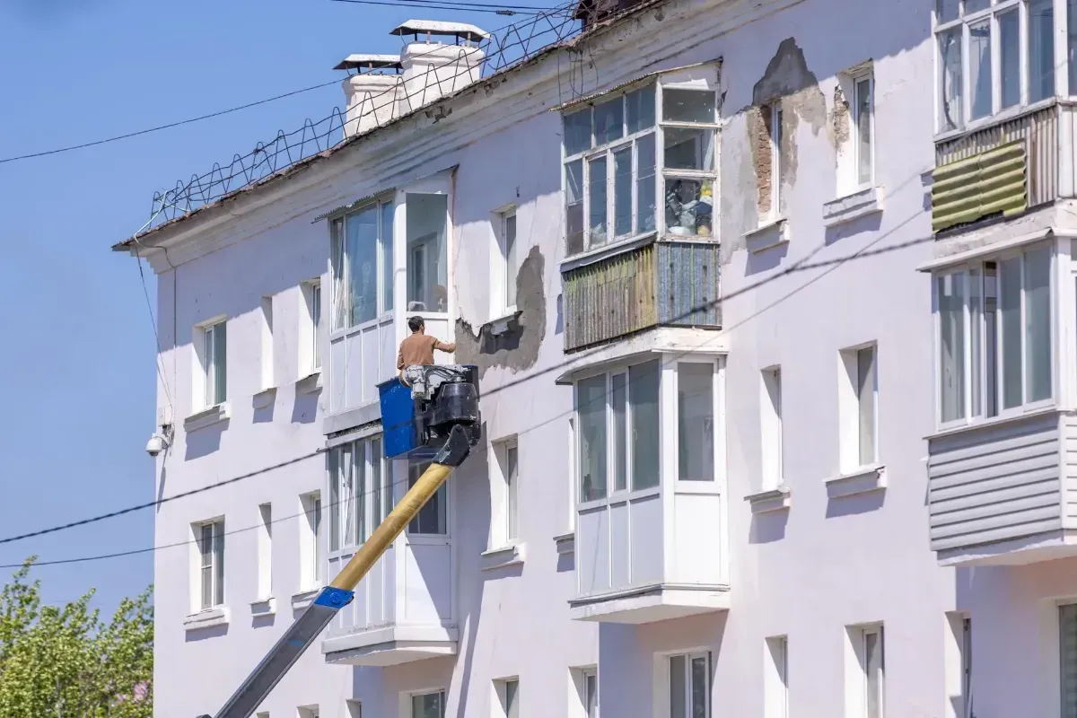 Worker on a cherry picker repairing a white apartment building facade