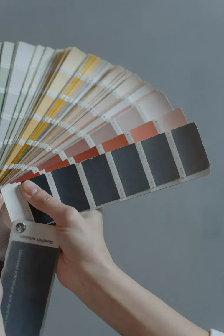 Hand holding a fan of paint color swatches against a gray background