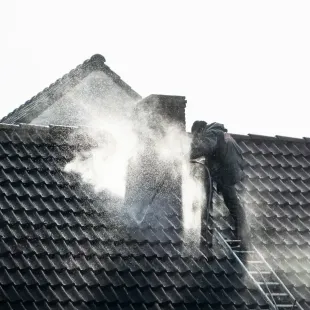 Workers washing a dark tiled roof with high-pressure water spray