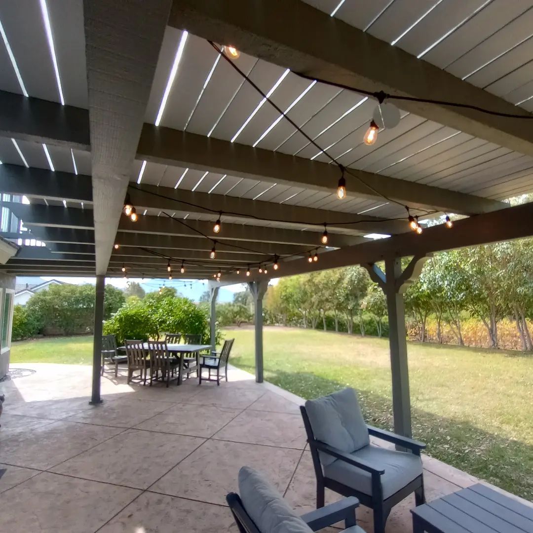 Covered patio with string lights, outdoor dining table, and chairs overlooking a grassy backyard.