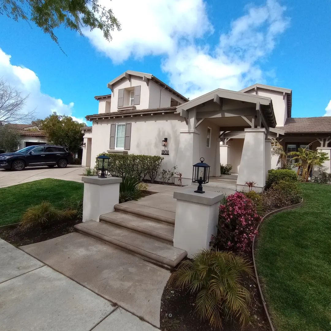 Front view of a beige stucco house with steps, a covered entry, landscaped yard, and a parked car in the driveway