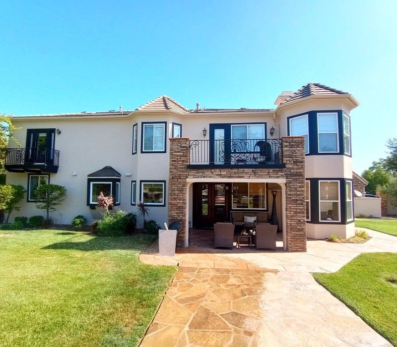 Large two-story house with a grassy yard, stone walkway, and covered patio under a bright blue sky