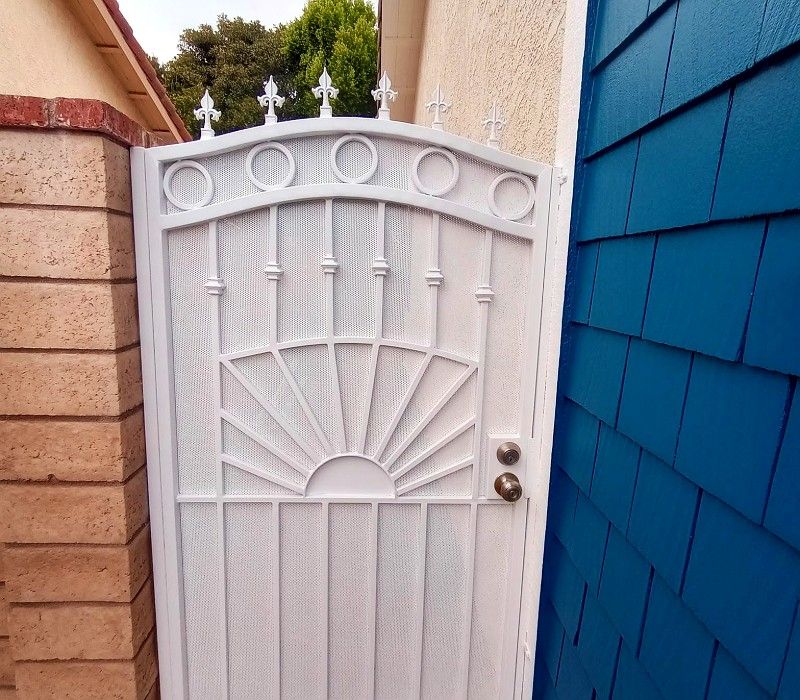 White metal gate between tan and blue walls, featuring an ornate fan design and a round door knob.