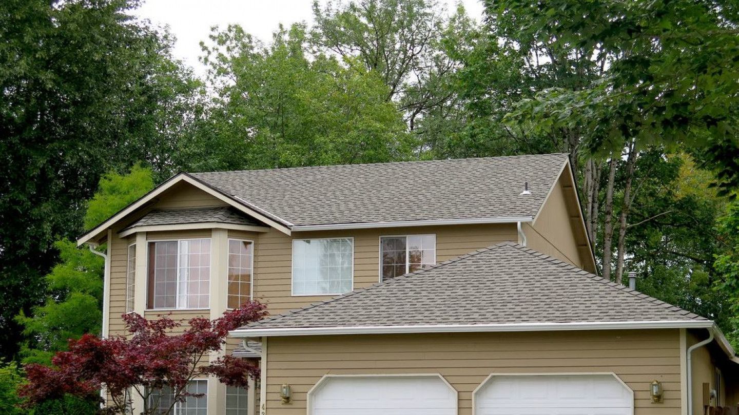 A house with two garage doors is surrounded by trees