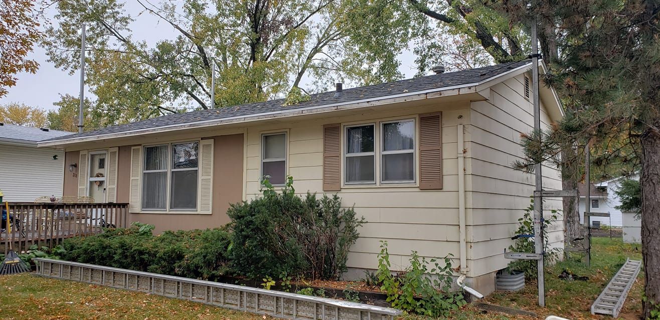 A small white house with a gray roof and brown shutters