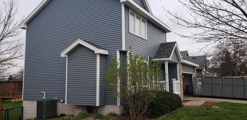 A blue house with white trim and a black roof is sitting on top of a lush green lawn