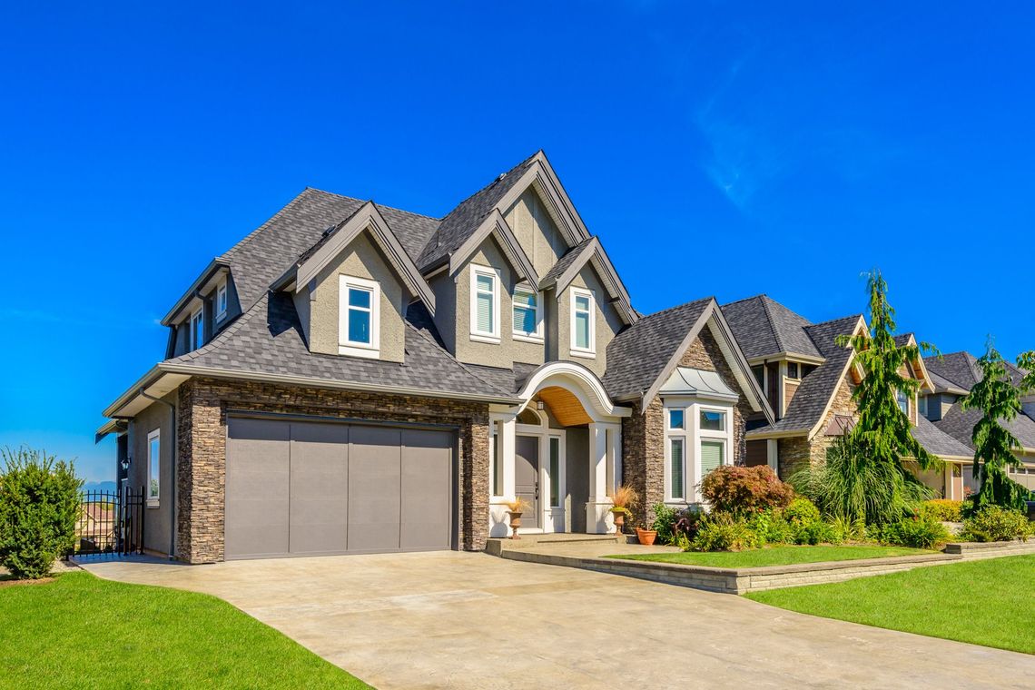 A large house with a gray garage door and a blue sky in the background