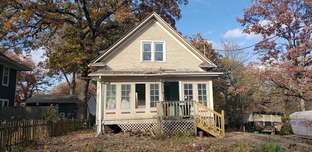 A small white house with a yellow deck is sitting in the middle of a field