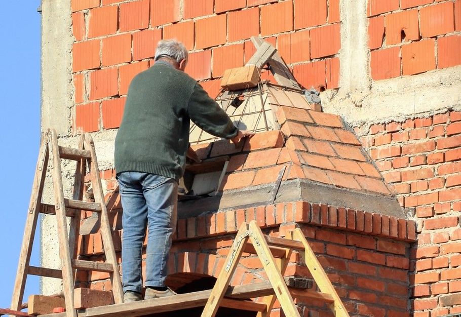 Worker on a ladder repairing a brick wall beside a chimney